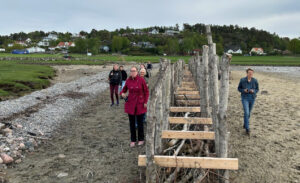 En liten grupp människor rör sig vid en träbyggnad på en strand.
